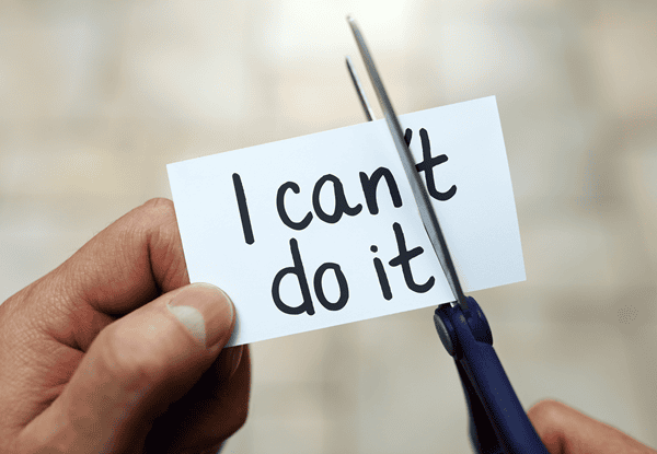 Ein Zettel auf dem "I cant't do it" steht, wird von einer Hand festgehalten und von einer Scheere zerschnitten