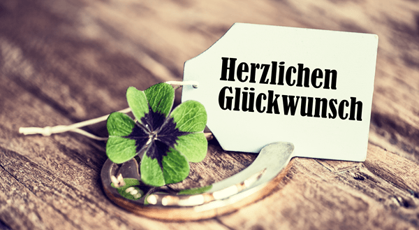 Ein Kleeblatt das auf einem goldenen Hufeisen liegt, dahinter ein Etikett auf dem steht "Herzlichen Glückwunsch"
