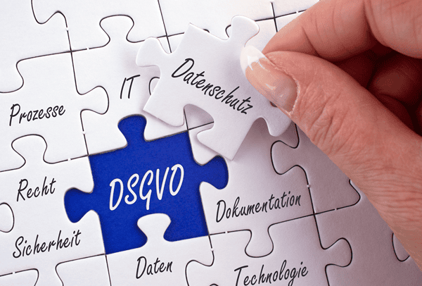 Ein weißes Puzzle, in der Mitte hält eine Hand ein Puzzleteil fest auf dem "Datenschutz" steht, in der Lücke in der das Puzzleteil fehlt steht "DSGVO"