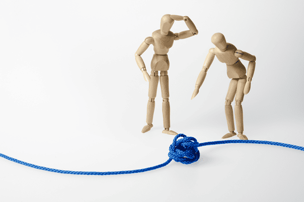 Zwei Gliederpuppen, die vor einer blauen Schnur mit einem Knoten stehen, eine zeigt darauf, die andere hat die Hand am Kopf, eine Hand an der Hüfte