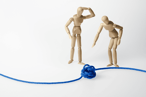 Zwei Gliederpuppen, die vor einer blauen Schnur mit einem Knoten stehen, eine zeigt darauf, die andere hat die Hand am Kopf, eine Hand an der Hüfte