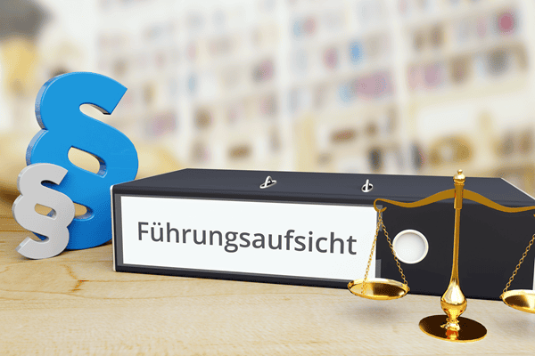 Ein Aktenordner mit der Aufschrift "Führungsaufsicht", davor eine Balkenwage, dahinter zwei Paragraphenzeichen