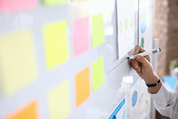 Eine Tafel mit bunten Post-its, eine Hand die etwas auf die Tafel schreibt